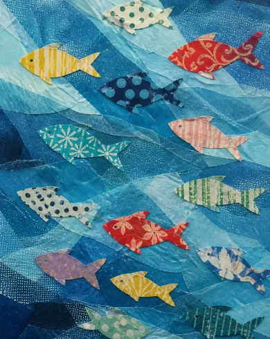 Handmade paper collage / dimensional assembly artwork depicting fish cut from varied gift wrap swimming through layers of translucent blue tissue. The vertical composition keeps the subject clear with tactile material and natural-light detail.