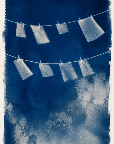Sun-exposed cyanotype / cotton rag paper artwork depicting cloth scraps, clothespins and thread forming a wordless cyanotype notation of wind. The vertical composition keeps the subject clear and preserves authentic craft texture.